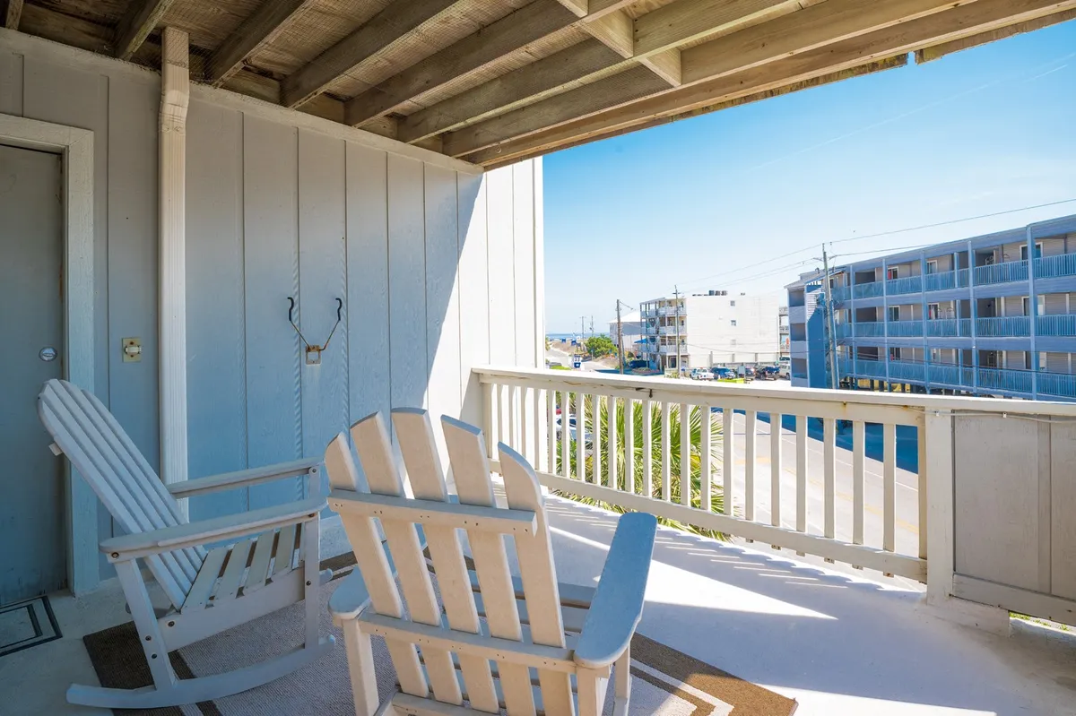 This image features a tranquil porch with classic rocking chairs positioned to face an open view. The scene includes a weathered wood ceiling overhead and soft natural light. The porch exudes a calm, coastal vibe and invites quiet moments of reflection or conversation, while providing a visual connection to the outdoors and street below.