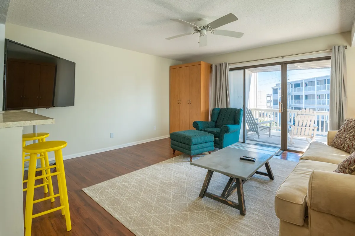 This image features a cozy living area with a sofa, coffee table, and armchair arranged around a sliding glass door that opens to the outside. Natural light pours in, hinting at the connection between interior comfort and the outdoor environment, while the setup encourages both relaxation and socializing. The sliding glass door visually suggests access to a balcony or outdoor views, supporting the idea of flexible living and easy transition from work to leisure.