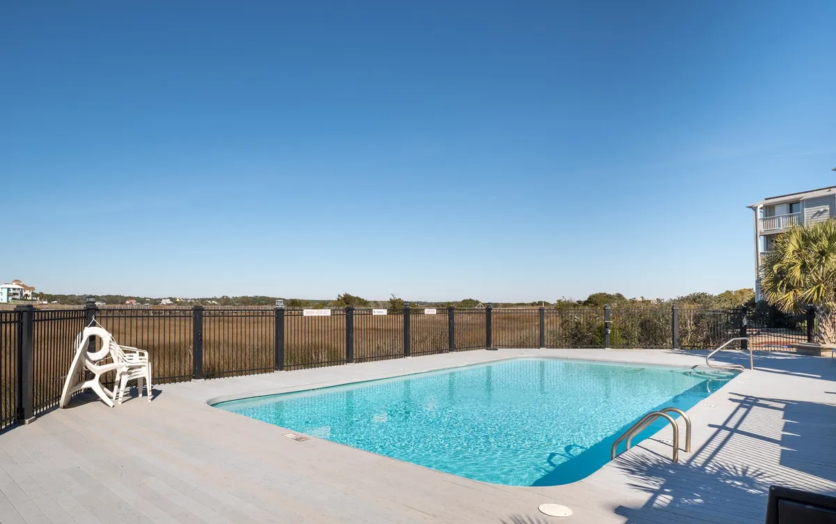 This image features the community swimming pool surrounded by a fenced area, with inviting lounge chairs positioned for relaxation. The landscape view beyond the pool provides a tranquil setting, and the scene evokes a calm yet social atmosphere where guests can swim, sunbathe, or gather for casual conversations.