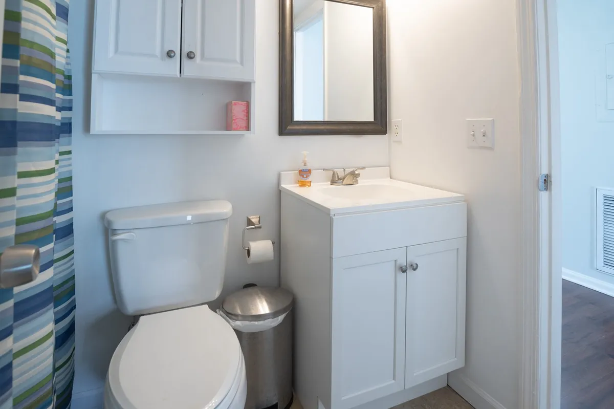 A bright, fresh bathroom with a white sink, mirror, and colorful shower curtain. The layout is simple and practical, emphasizing cleanliness and comfort.