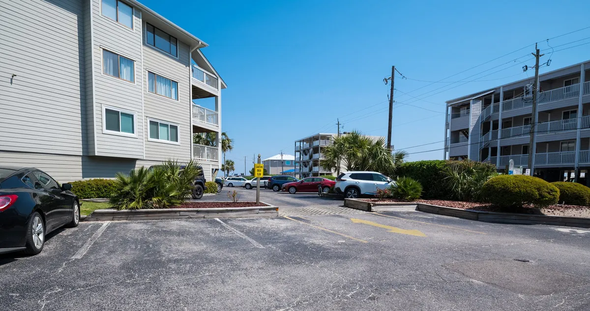 Two apartment buildings with a dedicated parking area in the foreground, flanked by palm trees under a clear blue sky. The scene suggests convenience and accessibility for short-term residents, with a relaxed outdoor vibe.