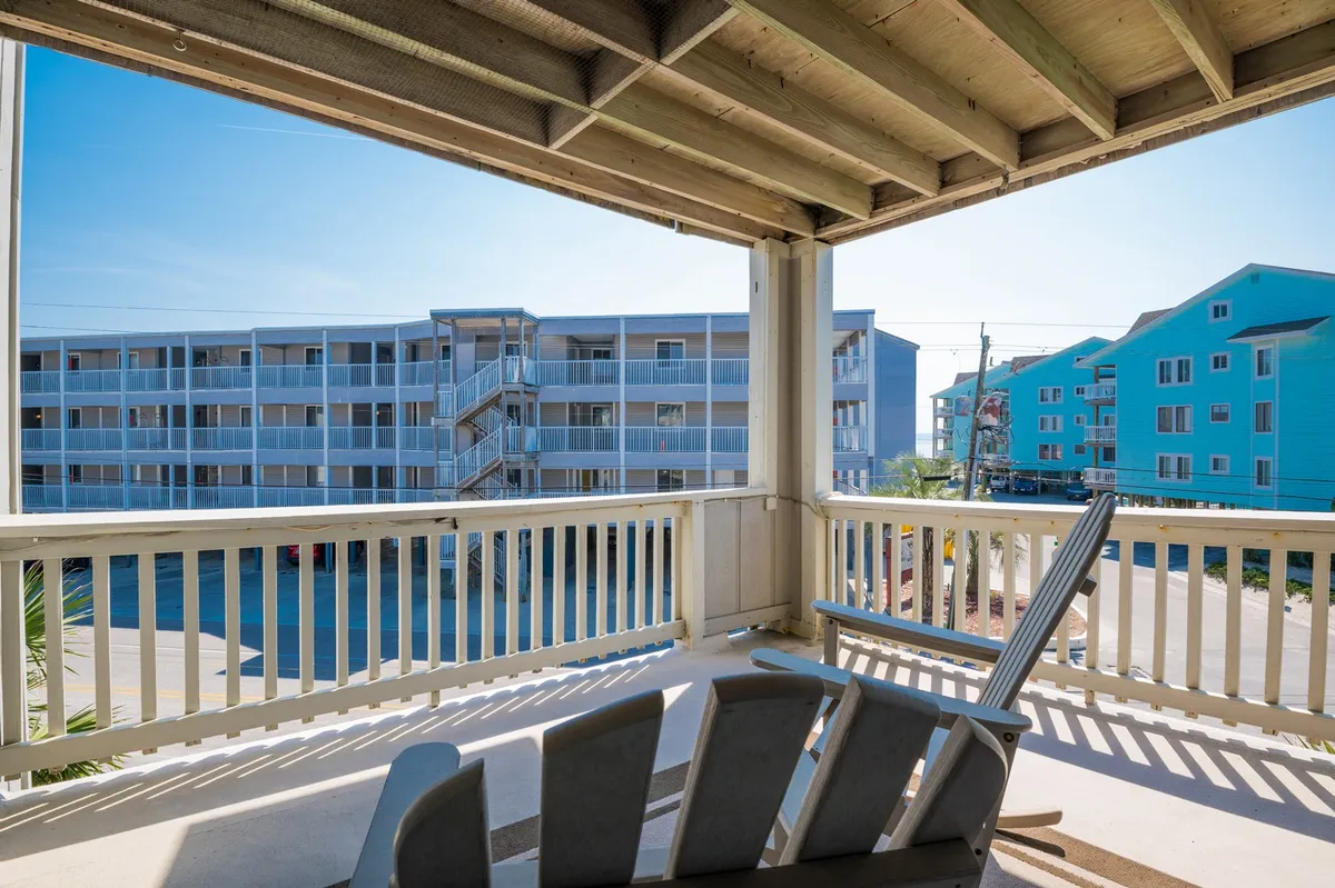 An exterior shot from a private balcony with a railing and a cozy lounge chair, overlooking nearby coastal buildings. The view captures the tranquil ambiance, with open skies and hints of the ocean breeze, creating a relaxing space ideal for unwinding after outdoor adventures.
