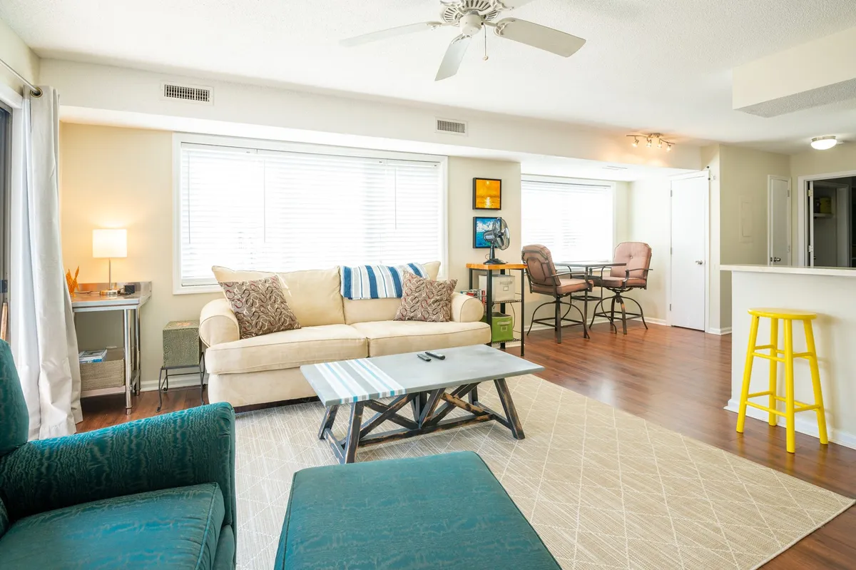 The image showcases a bright, comfortable living space featuring a plush sofa, a modern coffee table, a small dining area, and a large window that invites natural light, all arranged to create a warm and inviting atmosphere perfect for relaxing, sharing meals, or catching up on work.