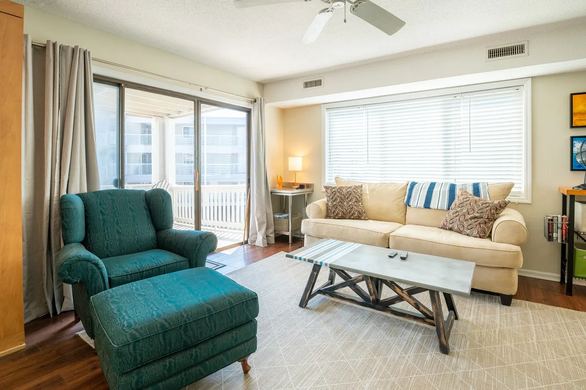A comfortable beige sofa and turquoise armchair create an inviting seating area around a wooden coffee table. Sunlight streams in, setting the scene for laid-back afternoons or spontaneous get-togethers. The arrangement is perfect for both unwinding after local outings and settling in for work with WiFi and Alexa support.